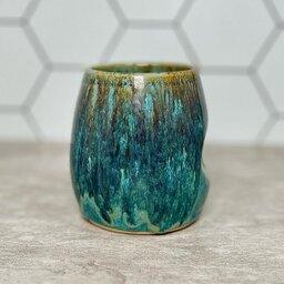 A ceramic tumbler coated with a glossy turquoise glaze, giving it a smooth and shiny finish