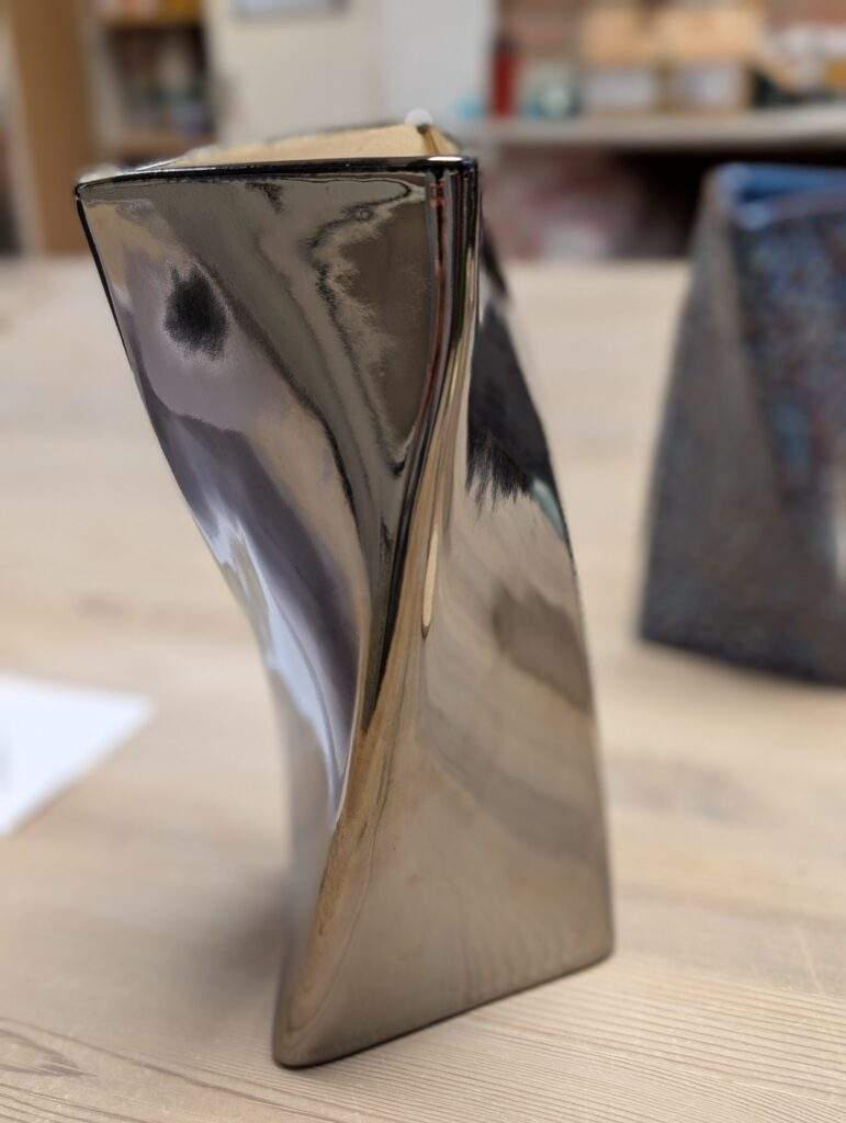 Twisted ceramic vase by Dave Colett with a reflective silver Palladium glaze, shown next to a quote describing the cone 6 firing.