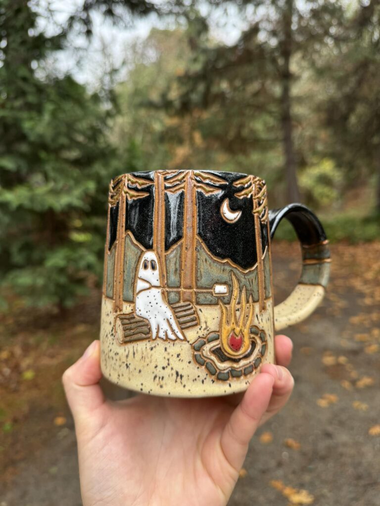 Handmade ceramic mug by Madison Salsgiver with forest scene and ghost design glazed in earthy tones using Mayco Smoke and Macadamia on speckled brownstone at cone 5