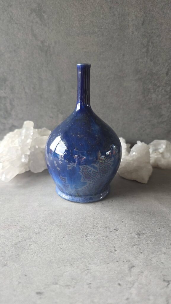 mall round stoneware vase by Kelsey Schroeder with a narrow neck, glazed in AMACO Blue Starlight with Cobalt Celadon, showing deep blue tones with crystalline star-like patterns at cone 6.