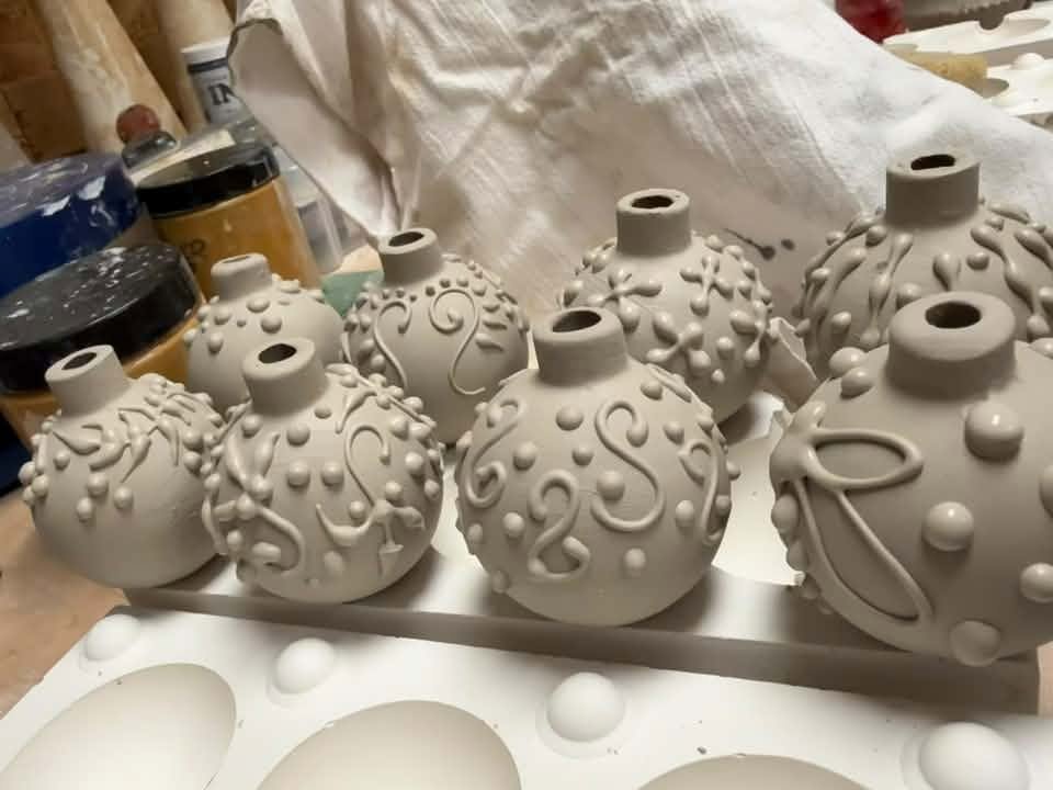 A group of unglazed slip-trailed ceramic baubles with individual raised patterns on a pottery workbench.